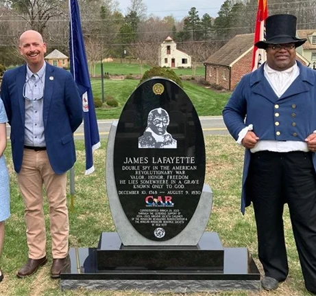 Monument dedicated to James Lafayette with two individuals standing beside it, one in modern attire and the other in historical costume.
